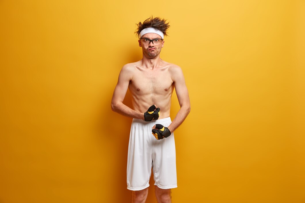 funny-sporty-nerd-shows-biceps-muscles-wears-sport-gloves-shorts-has-serious-strict-expression-wants-have-strong-body-doesnt-want-be-weak-poses-against-yellow-wall_273609-39560.jpg